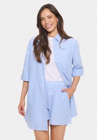 Blå och vit randig skjorta med knappar och uppvikta ärmar, ihop med matchande randiga shorts. Mjuk tyg med avslappnad passform och sidfickor.