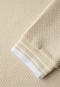 Primer plano de tela beige texturizada con patrón de tejido tipo gofre y puño con franjas horizontales blancas y amarillas.