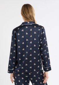 Granatowy jedwabny zestaw piżamowy z powtarzającym się wzorem psa, białym obszyciem na kołnierzu i mankietach oraz gładką, błyszczącą fakturą.