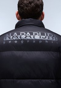 Padded černá bunda s velkým, lesklým logem "NAPAPIJRI geographic" na zádech, s hladkým, lesklým povrchem.