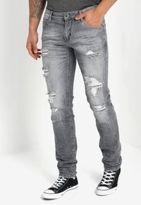 Jeans de mezclilla gris con detalles desgastados, que presentan desgarros y un corte ajustado. Combinados con zapatillas altas negras.