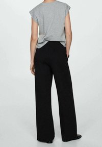 Chemise grise à manches courtes associée à un pantalon noir à taille haute et jambes larges. Le tissu semble doux, avec une texture lisse et un design simple.