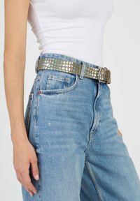 Metallinen kudottu vyö, jossa on neliökuvioita vaaleansinisissä ja hopeansävyissä. Varustettu suorakulmaisella hopeavöillä, yhdistetty korkeavyötäröisiin farkkuihin.