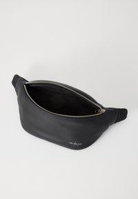 Zwart leren heuprugzak met een ritssluitingen aan de bovenkant, een soepele textuur en een Calvin Klein Jeans logo aan de zijkant. Bevat twee zijaccentdetails.