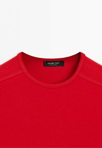 Red crew neck shirt with visible stitching on shoulders and a black label reading "Massimo Dutti Made in Morocco."