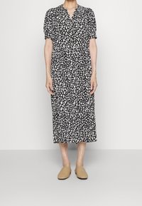 Schwarz-weißes Leopardenmusterkleid mit kurzen Ärmeln, einem V-Ausschnitt und einem schichtweisen Rock. Getragen mit hellbraunen, geflochtenen Slippers.