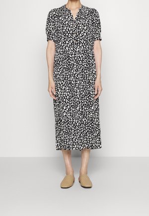 Abito a stampa leopardata in bianco e nero con maniche corte, scollo a V e gonna a strati. Indossato con ciabatte in tessuto intrecciato di colore marrone chiaro.