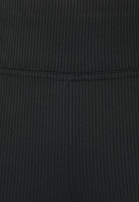 Tecido preto com nervuras e uma textura suave, apresentando uma cintura larga e costura visível ao longo das costuras.