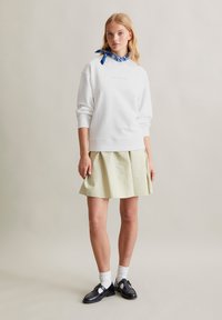 Witte sweatshirt met verlaagde schouders, gecombineerd met een lichtgroene plissé minirok. Zwarte schoenen met witte sokken en een blauwe geblokte halsdoek.