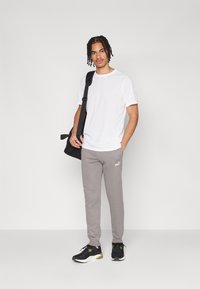 Witte t-shirt met korte mouwen, grijze sweatpants met logo, zwarte sneakers en een zwarte schoudertas. Effen kleuren, relaxte pasvorm, casual stijl.
