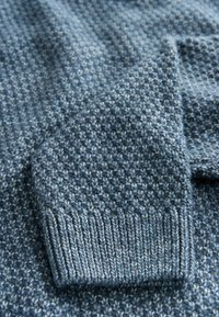 Sweter z dzianiny w różnych odcieniach niebieskiego z teksturowanym wzorem. Ma ściągacz na mankietach, co dodaje mu charakteru oraz sprawia, że wygląda na miękki i ciepły.