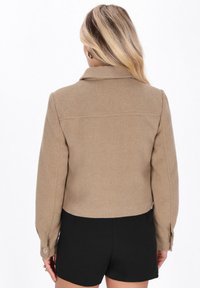 Giacca beige a coste, tagliata, con colletto e polsini abbottonati, abbinata a pantaloni corti neri. Design pulito e minimalista.