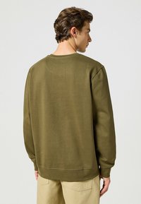 Oliwkowy sweter z okrągłym dekoltem, długimi rękawami i ściągaczami. Posiada płaskie szwy i luźny krój. Wykonany z gładkiej mieszanki bawełny.