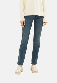 Jeans rectos azules con un lavado medio, combinados con un suéter suelto crema y mocasines crema de plataforma. Presenta un diseño clásico de cinco bolsillos.
