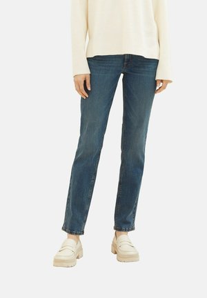 Jean droit bleu avec une teinte moyenne, porté avec un pull crème ample et des mocassins plateforme crème. Comprend un design classique à cinq poches.
