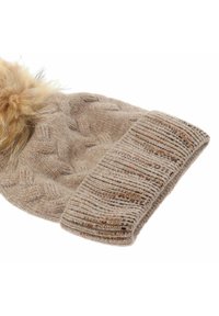 Beżowa dzianinowa czapka z teksturowanym wzorem warkocza, z podwiniętym prążkowanym mankietem i puszystym pomponem na górze; posiada subtelne akcenty z metalicznej nici.