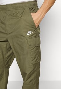 Oliivinvihreät cargo-housut joustavalla vyötäröllä, sivutaskuilla ja valkoisella Nike-logolla yläreidessä. Kevyt kangas.