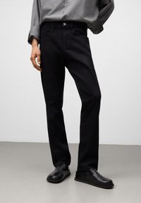 Jeans in denim nero a gamba dritta, con cinque tasche, chiusura a bottone e cuciture discrete. Abbinati a scarpe slip-on nere.