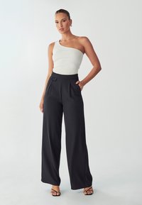 Witte geribbelde top met één schouder, gecombineerd met zwarte high-waisted wijde broek met plooien en een zijknopdetail.