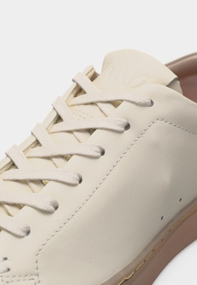 Λευκός-εκρού δερμάτινος αθλητικός παπούτσι με λευκά κορδόνια, ραφές και μπεζ καουτσούκ σόλα, εμφανίζεται από κοντινή γωνιακή άποψη.
