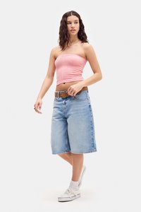Haut rose sans bretelles avec un motif texturé, shorts en denim bleu à mi-cuisses, ceinture brune, baskets blanches et chaussettes blanches rasta.