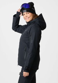 Black ski jacket with a hood, featuring multiple zippered pockets, a smooth texture, and a woman wearing ski goggles and a black beanie.