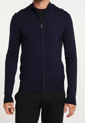 Chandail zippé marine avec col montant, design ajusté, poignets et ourlet côtelés. Fabriqué dans un tissu doux et texturé.