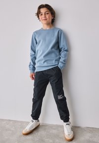 Lichtblauwe sweatshirt met structuur, zwarte cargobroek met zakken en witte sneakers met beige zolen. Eenvoudige geometrische patronen op de sweatshirt.
