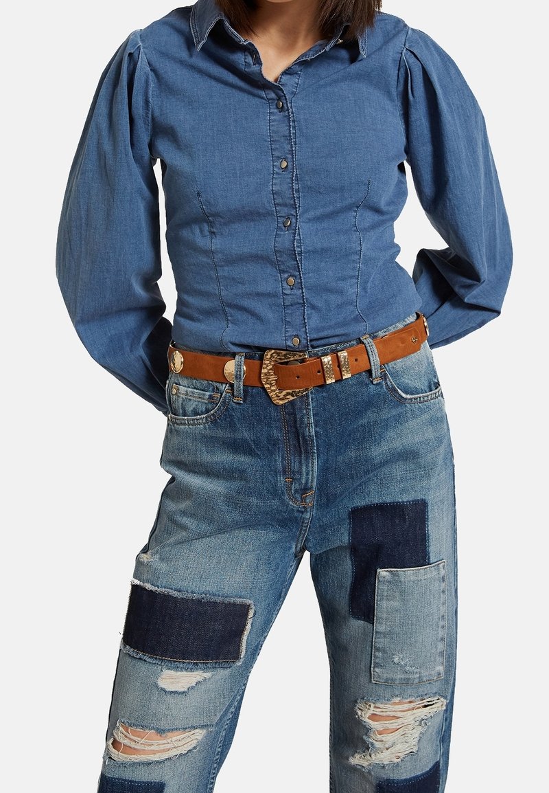 Denim-painettu napituspaita puffipäillä, yhdistettynä kulutettuihin farkkuihin, joissa on erilaisia sinisen sävyjä ja ruskea vyö.