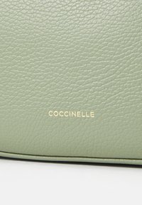 Žalias tekstūruotas odinis krepšys su lygiu paviršiumi, su auksiniu "Coccinelle" logotipo akcentu. Forma stačiakampė su suapvalintais kraštais.