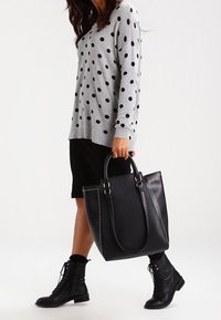 Svart läderhandväska med nitar, kombinerad med en grå prickig tröja och svart kjol; kängor fulländar outfiten.