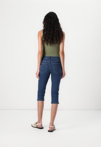 Un capri en denim avec une taille ajustée, des ourlets roulés et deux poches arrière. Le haut est un débardeur ajusté de couleur olive. Texture légère et design décontracté.