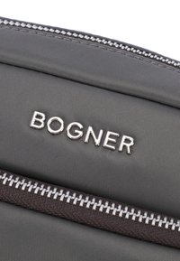Šedá nylonová taška se stříbrným logem "BOGNER". Obsahuje tmavě hnědý zip s kovovými zuby a texturovanou tkaninou. Minimalistický design.