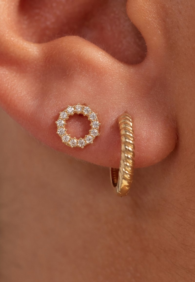 Goldene Creolen und runde Ohrstecker, die klare Edelsteine in einer Krappenfassung zeigen. Die texturierte Oberfläche des Goldes an der Creole fügt Detail hinzu.