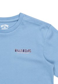 Ljusblå bomulls-T-shirt med ribbad rundhals och en tryckt logotyp i mörkblått och rosa på vänster bröst. Mjuk textur.