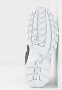 Czarny but sportowy z białą gumową podeszwą. Podeszwa zewnętrzna ma teksturowany wzór zwiększający przyczepność, z wygrawerowanym logo w centrum.