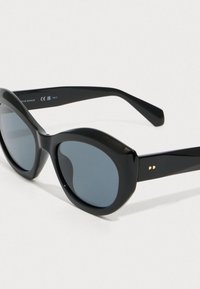 Czarne, błyszczące, oversize'owe okulary przeciwsłoneczne w kształcie owalu z ciemnymi, przyciemnianymi soczewkami i subtelnym złotym logo na zauszniku, wyeksponowane na białym tle.