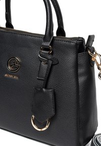 Borsa a mano in pelle nera con due manici superiori, dettagli in hardware dorato, un anello circolare e una superficie testurizzata. Presenta una tracolla rimovibile.