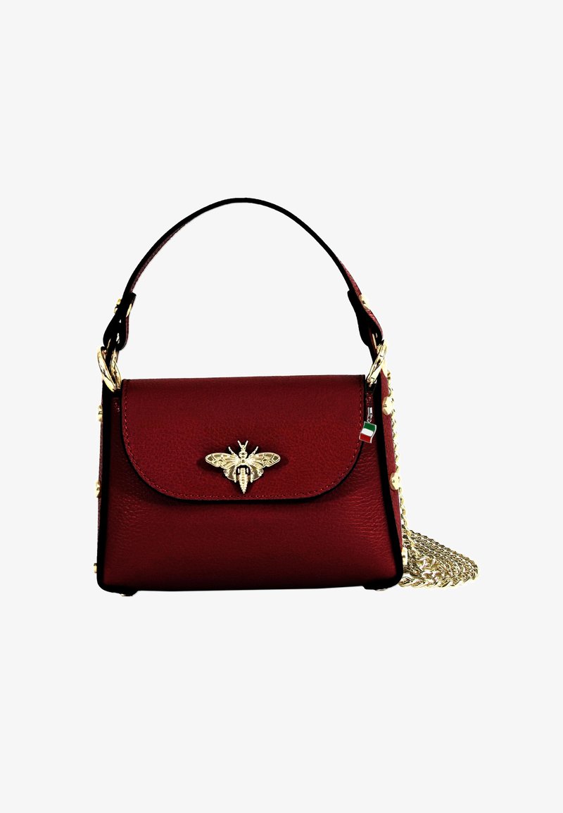 Sac à main en cuir rouge avec un rabat supérieur incurvé, un emblème en or de abeille, une bandoulière en chaîne et des accessoires décoratifs le long des bords. Surface texturée.