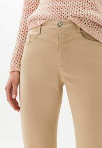 Pantalon en denim beige à coupe slim, doté de poches avant, d'une fermeture par bouton et de détails cousus le long des coutures.