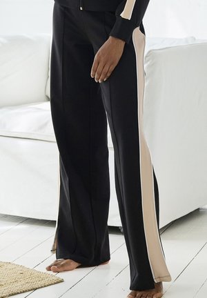 Schwarze Hose mit cremfarbenen Seiteneinsätzen, flared Design und weichem Stoff. Auffällige weiße Paspeln entlang der Kanten.