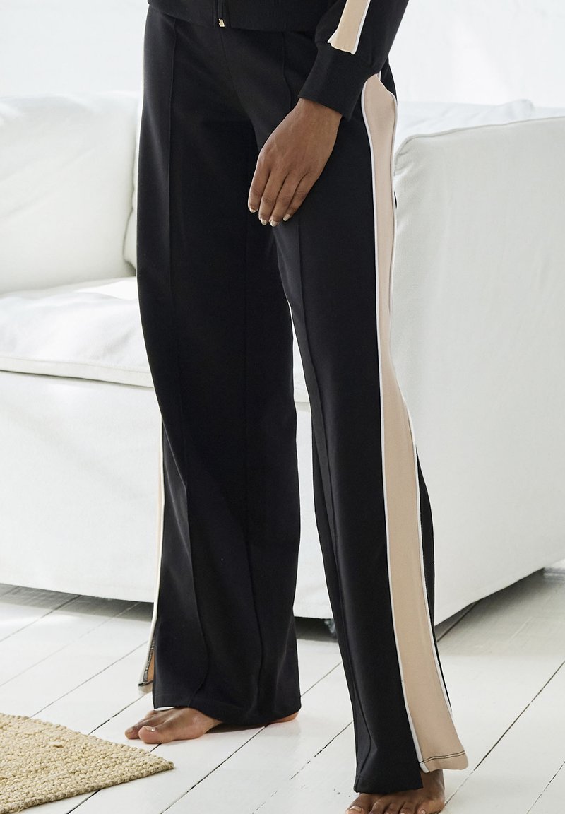 Schwarze Hose mit cremfarbenen Seiteneinsätzen, flared Design und weichem Stoff. Auffällige weiße Paspeln entlang der Kanten.