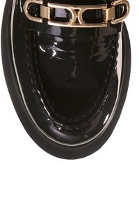 Mocassin en cuir verni noir avec un bout arrondi, accent en métal doré et détail texturé. Présente un contour de couture blanc contrastant.