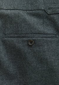 Grau gestreifter Stoff mit einer strukturierten Webart, ausgestattet mit einer Paspeltasche und einem einzelnen schwarzen Knopf in der Mitte, der Funktionalität und Design verbessert.