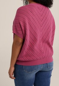 Stickad T-shirt med kort ärm i stark fuchsia, med diagonala texturerade ränder och en ribbad nederkant, parat med figurnära blå jeans.