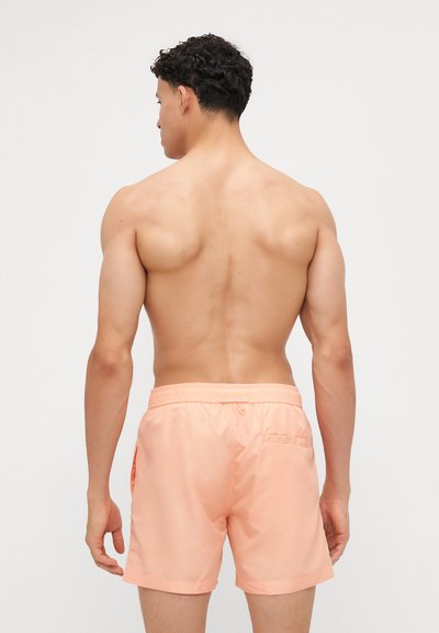 Lys fersken svømmet trunks laget av glatt stoff, med elastisk livakt, og en liten baklomme med et elegant design.