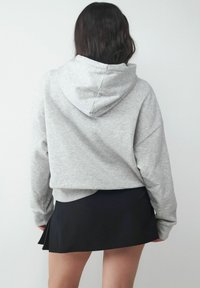 Szara skrócona bluza z kapturem, z szerokimi rękawami i teksturowanym wykończeniem, w połączeniu z czarną dopasowaną spódnicą o plisowanym fasonie.