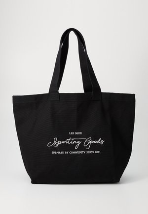 Sac cabas noir avec longues anses, avec texte blanc « LES DEUX Sporting Goods INSPIRED BY COMMUNITY SINCE 2011 » sur le devant.