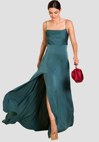 Abito da sera in satin teal con corsetto aderente, spalline sottili e uno spacco alta coscia. Abbinato a una clutch rossa in satin e tacchi platform.