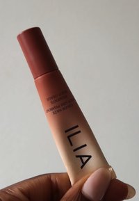 Pigment multi-usage ILIA Color Haze dans un tube ; dégradé d'orange à nude avec une finition mate. Dispose d'une pointe inclinée et d'un texte noir vif.